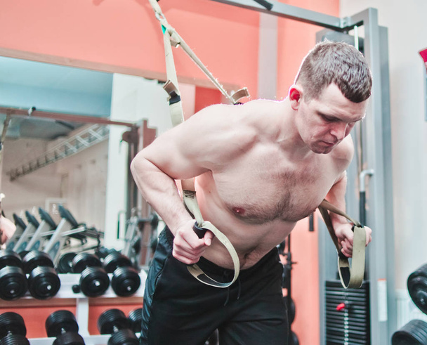 Starker Mann macht Crossfit-Liegestütze mit Fitnessgurten im Fitnessstudio  - Foto, Bild