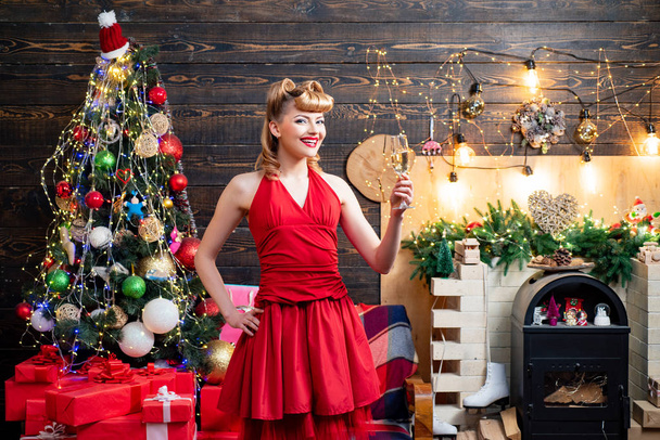 Beautiful blonde girl in evening dress smiling and holding glass of champagne. Pretty girl wearing in red Christmas dress. Beautiful New Year and Christmas scene. - 写真・画像