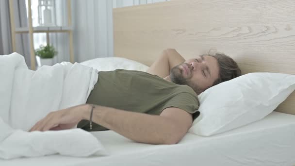 Hombre joven cansado con dolor de espalda mientras duerme en la cama
 - Imágenes, Vídeo