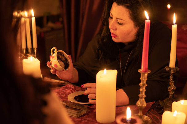 Wróżka Kobieta w ciemnym pomieszczeniu z mnóstwem świec daje wyjaśnieniu przyszłości i przewidywania losu do klienta z filiżanką kawy gęste osady - Zdjęcie, obraz