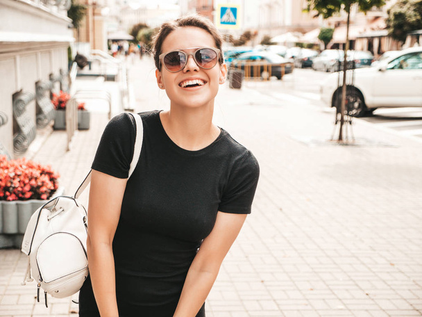 Portrait of beautiful smiling hipster model dressed in summer clothes. Trendy girl posing in the street background in sunglasses. Funny and positive woman having fun - 写真・画像
