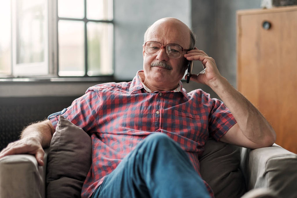 Emekli İspanyol adam oturma odasında otururken telefonda konuşurken. - Fotoğraf, Görsel