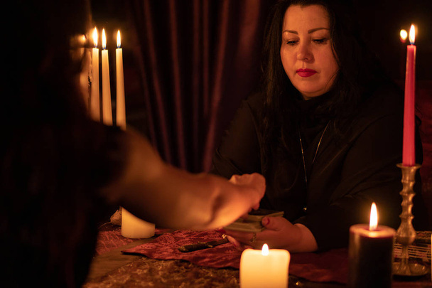 Женщина-предсказательница в темной комнате с кучей свечей угадывает на колоде карт Таро
 - Фото, изображение
