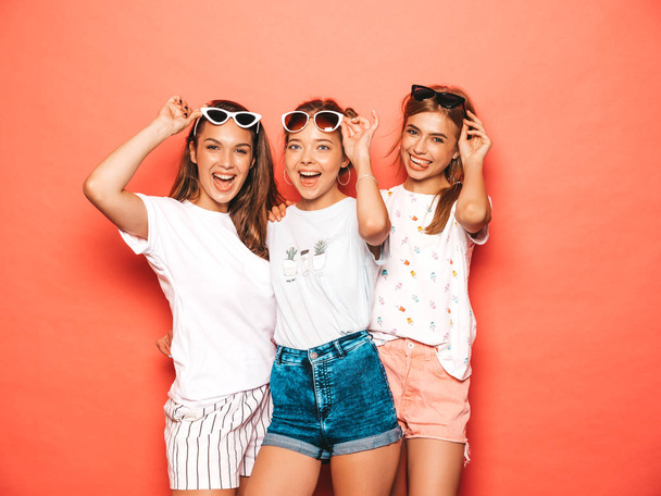 Three young beautiful smiling hipster girls in trendy summer clothes. Sexy carefree women posing near pink wall in studio. Positive models going crazy and having fun in sunglasses - Foto, Imagem