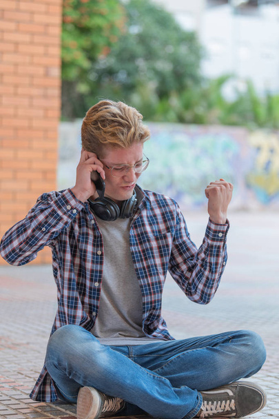 Un ragazzo seduto sul pavimento con un atteggiamento molto positivo mentre parla al telefono
. - Foto, immagini
