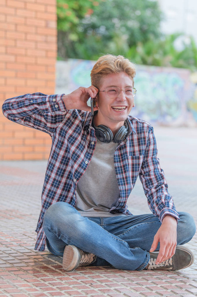 Μια κάθετη εικόνα ενός χαμογελαστή νεαρού άντρα που κρατά το τηλέφωνο με το ένα χέρι. - Φωτογραφία, εικόνα