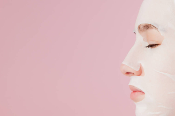 Beautiful young woman is applying a cosmetic tissue mask on a fa - Φωτογραφία, εικόνα