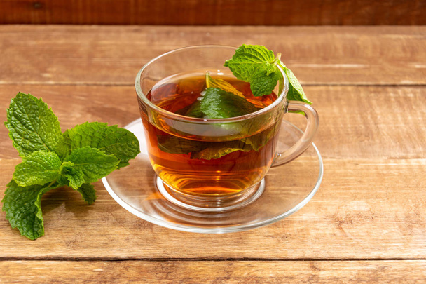 Tea with mint in a glass cup. In a cup and on a table mint leaves. - Foto, imagen