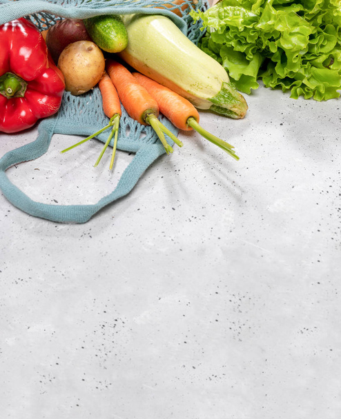 Fresh farm vegetables in string bag on grey concrete background with copy space.  - 写真・画像