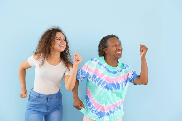 Portrait of African-American woman with her daughter dancing against color background - Foto, imagen