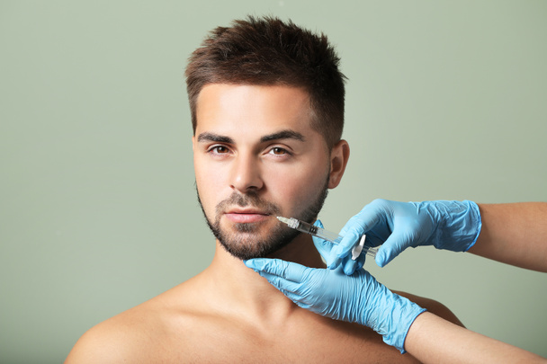 Handsome man receiving filler injection on color background - Фото, изображение