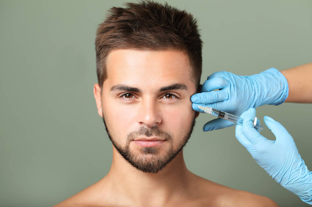 Handsome man receiving filler injection on color background - Zdjęcie, obraz