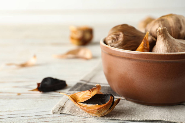 Bowl and black garlic on white wooden table. Space for text - Photo, Image