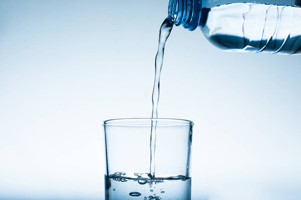 Выливание воды из бутылки в стекло на сером фоне. Освежающий напиток
 - Фото, изображение