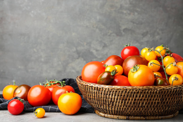 Fresh ripe tomatoes in wicker bowl on table against grey background. Space for text - Φωτογραφία, εικόνα
