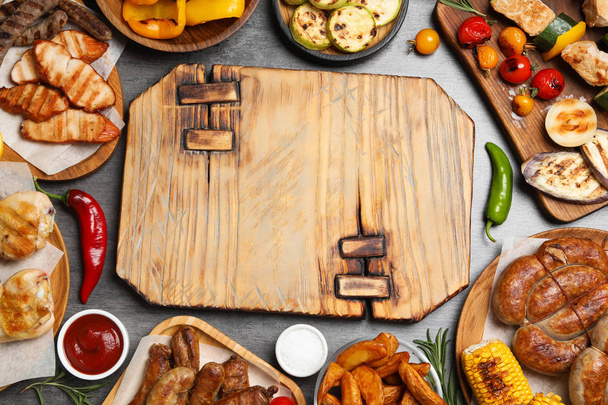 Frame of barbecued meat and vegetables on grey table, flat lay. Space for text - Фото, зображення