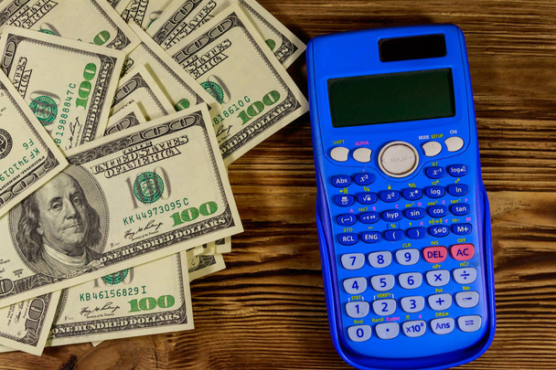 Calculator en Amerikaanse dollars bankbiljetten op houten tafel. Top View - Foto, afbeelding
