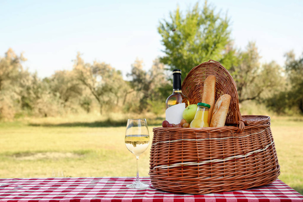 Wicker picnic basket with wine and snacks on table in park. Space for text - Foto, Bild