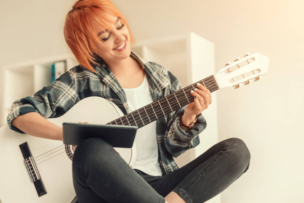 Cheerful female learning to play guitar at home - Fotografie, Obrázek