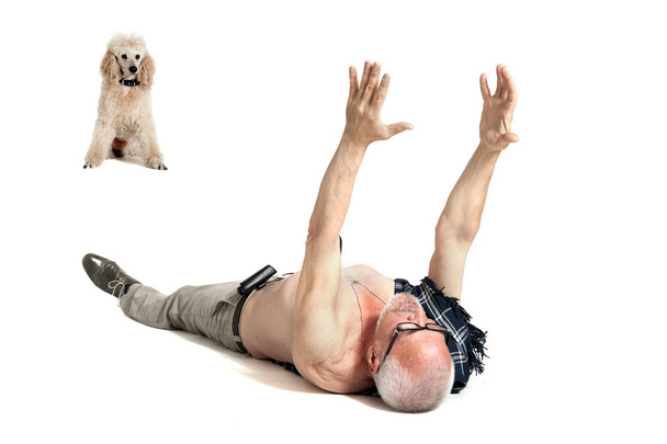 Mies koiran kanssa makaa lattialla ja nostaa kätensä ylös.
 - Valokuva, kuva
