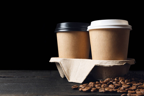 Twee papieren kopjes koffie in bekerhouder en koffiebonen op donker  - Foto, afbeelding