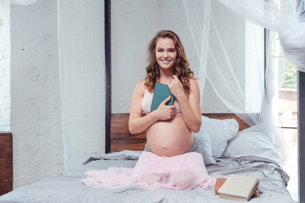 pregnancy and leisure concept - pregnant woman reading book in bed at home - Foto, Imagem