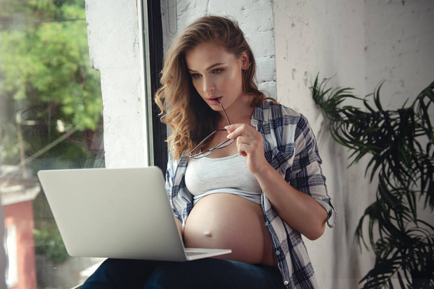 Zwangere vrouw gebruik van laptop computer om thuis te werken - Foto, afbeelding