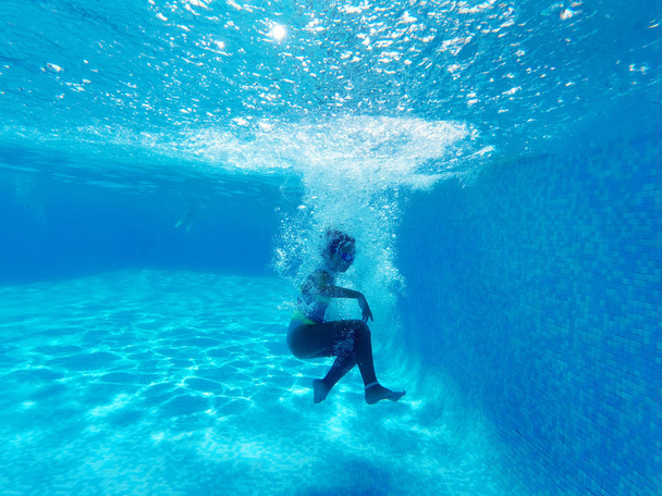 Kleines Mädchen von Blasen umgeben fällt in blaues Wasser des Swimmingpools - Foto, Bild