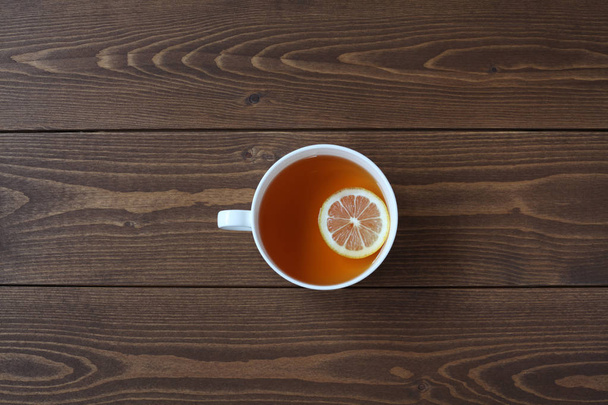 Чашка чая с нарезанным лимоном изолирована на деревянном столе
 - Фото, изображение
