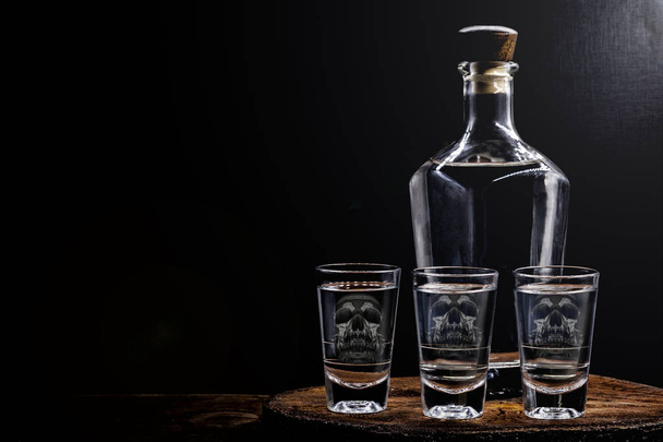 Beba botella y vaso con contenido de alcohol. Imagen de cráneo translúcido en vidrio. Alcoholismo, adicción o concepto de veneno
. - Foto, imagen