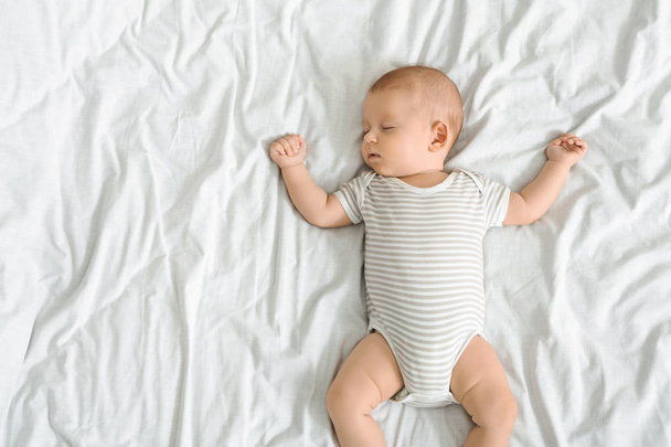 Cute infant baby in striped bodysuit sleeping on bed - Foto, Imagem
