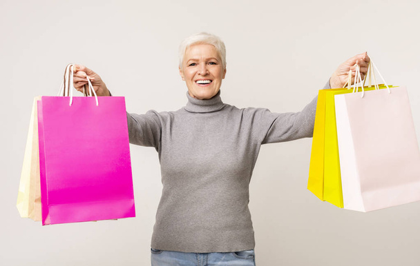 カラフルなショッピングバッグでポーズをとる幸せな高齢女性 - 写真・画像