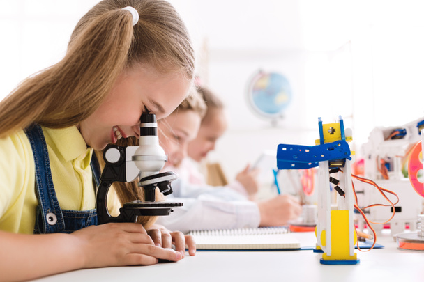 Mädchen betrachtet Mikroskop mit Roboter in der Nähe - Foto, Bild