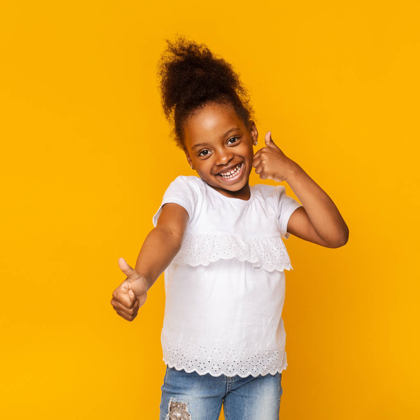 Ładny nieśmiały trochę Afro dziewczyna wskazując kciuki w górę i uśmiechnięty - Zdjęcie, obraz