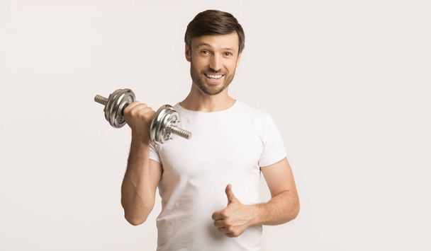 Handsome Man Holding Dumbbell Gesturing Thumbs-Up, White Background - Zdjęcie, obraz
