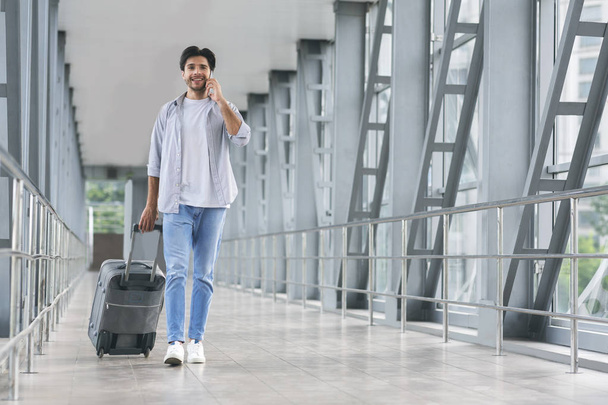 Young tourist talking on phone, walking in luggage in airport - Фото, зображення
