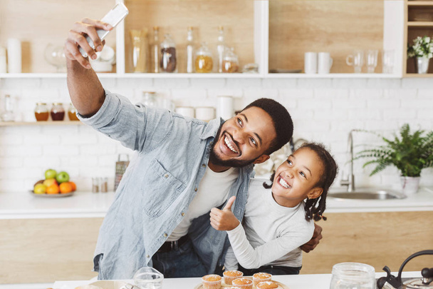 Чорний тато і дочка беруть селфі по телефону на кухні
 - Фото, зображення
