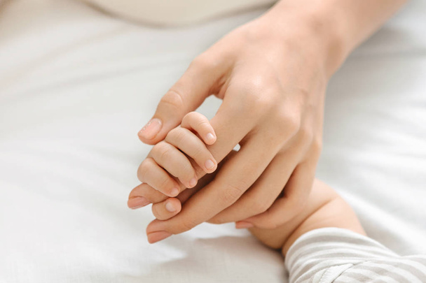 Крихітні пальці новонародженої дитини тримає руку матері, крупним планом
 - Фото, зображення