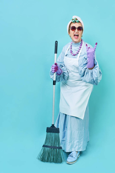 Уборка Леди Веселье. Пожилая домохозяйка развлекается с метлой. Полное тело изолировано
 - Фото, изображение