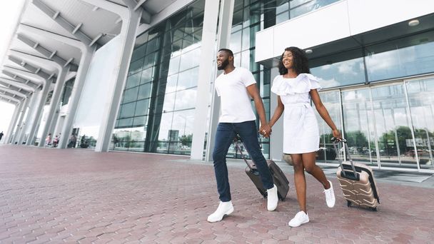 Heureux couple afro-américain courir avec des bagages à l'extérieur de l'aéroport
 - Photo, image