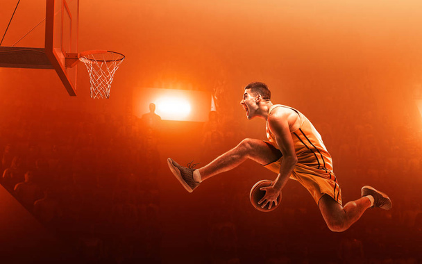 Баскетболист в спортивной форме на профессиональной спортивной арене в действии с мячом. Слэм данк. Прыжок. Красный прожектор
 - Фото, изображение