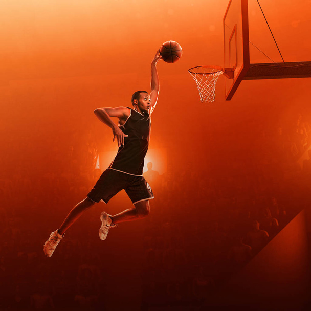 Jugador de baloncesto afroamericano en uniforme deportivo en una cancha de baloncesto profesional en acción con la pelota. Golpe de clavo. Salta disparado. Fondo rojo iluminado
 - Foto, imagen