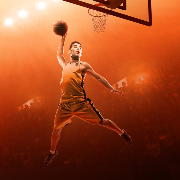 Basketball player in sports uniform on a professional basketball court in action with the ball. Slam dunk. Red floodlit background - Photo, Image