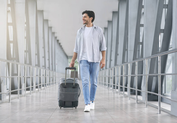 Young man walking in airport walkway with luggage - Foto, Imagem