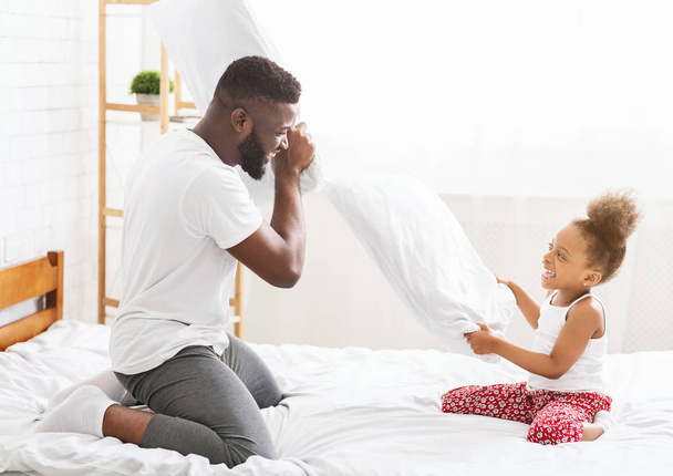 Afrykański ojciec i mała córka o poduszce walczyć na łóżku - Zdjęcie, obraz