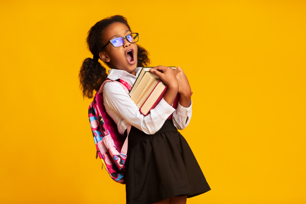 Νυσταγμένος Αφρικανός Αμερικανός μαθήτρια χασμουριέμαι μεταφορά βιβλίων, κίτρινο φόντο - Φωτογραφία, εικόνα