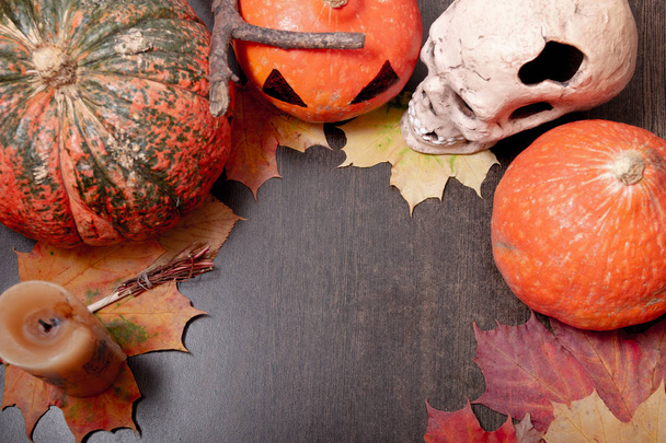 ceramic skull, candle, decorative broom and halloween pumpkins on a dark brown table background, autumn leaves and cones, copy space, top view - Foto, Imagem
