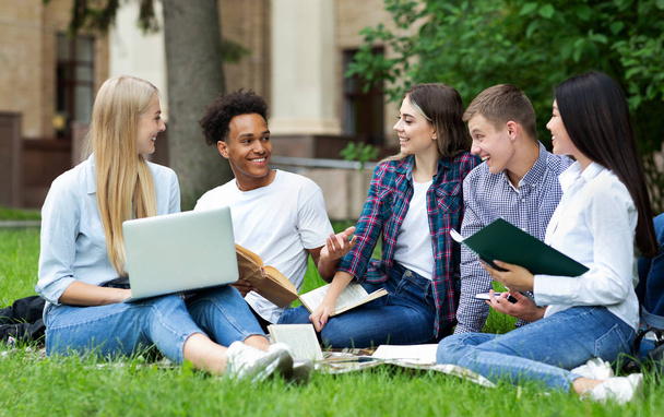 Возбужденные студенты отдыхают в кампусе, сидят на траве
 - Фото, изображение