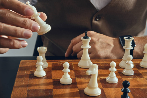 Egy férfi kezei, klasszikus barna mellényben és fehér ingben ül az asztalnál és sakkozik egyedül. Szürke háttér, közelkép. - Fotó, kép