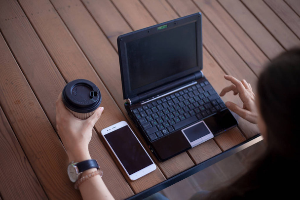 Jovens mãos femininas com uma manicura modesta, com grandes relógios de pulso, trabalham em um laptop, em pé em uma mesa de madeira
. - Foto, Imagem